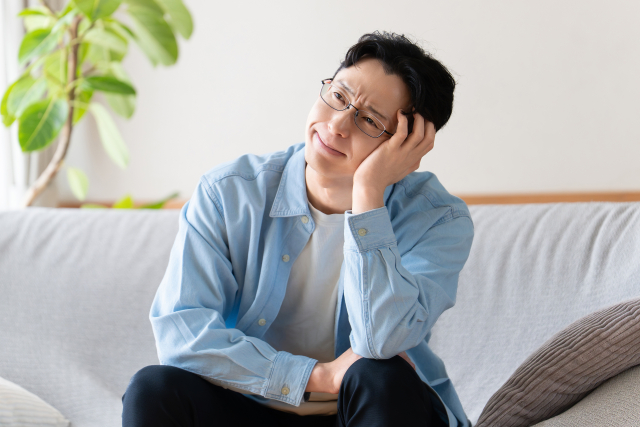 住まいの悩みを抱えて自宅のソファで考える男性
