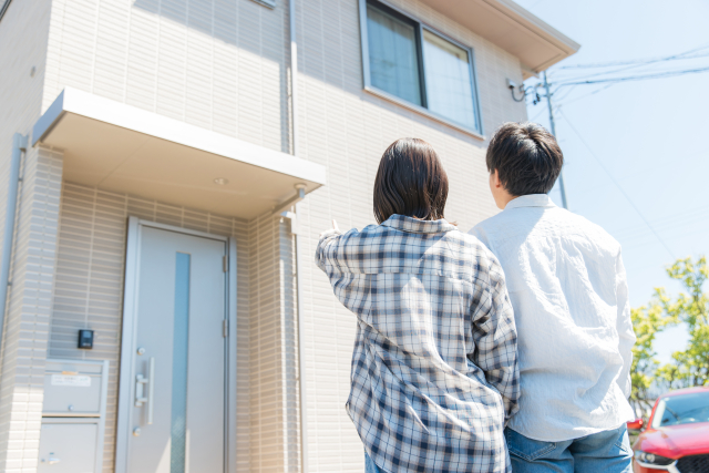 戸建て住宅の外観を確認する夫婦の後ろ姿